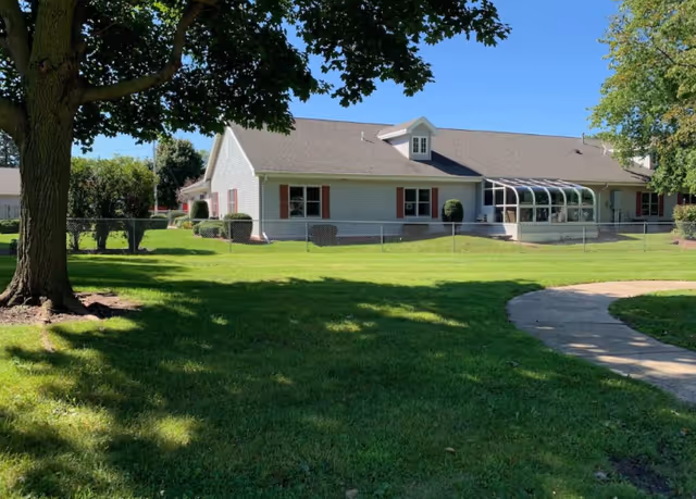 Single-story assisted living facility with a fenced green lawn and curved walkway.
