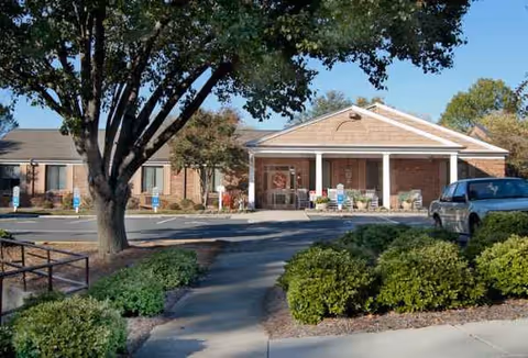 Front view of a brick senior living facility entrance with shrubs.