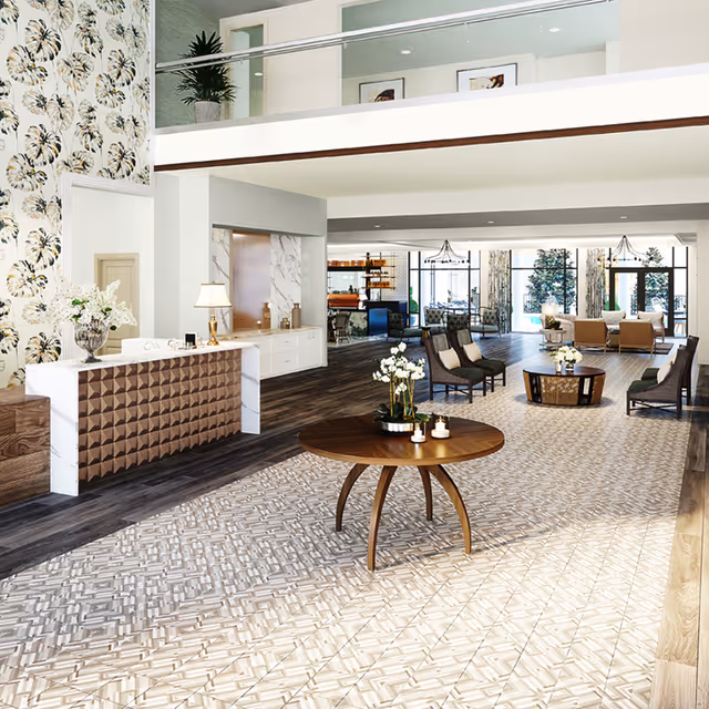 Spacious and modern assisted living facility lobby with a patterned tile floor, a round wooden table with flowers and candles, a reception desk with a lamp and flowers, comfortable seating areas with chairs and sofas, large windows letting in natural light, and decorative wallpaper on one wall.