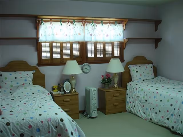 Small bedroom with two twin beds with polka-dot bedding, wooden headboards, matching nightstands and lamps under a window with wooden shutters.