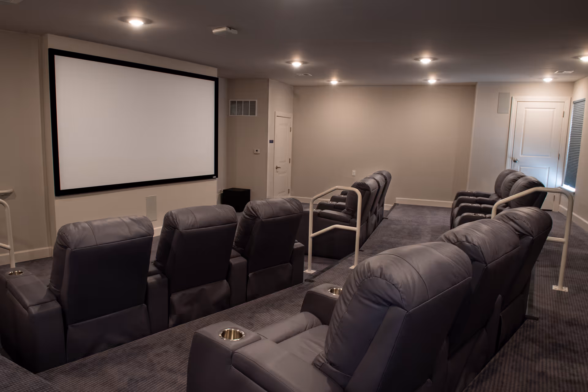 Small private theater room with rows of gray reclining seats facing a large white projection screen.