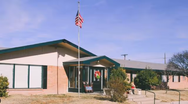 Exterior view of a brick assisted living facility with green trim, flagpole, and wreath.