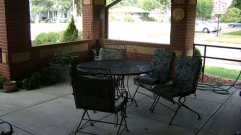 Covered outdoor patio with a round metal table and cushioned chairs.