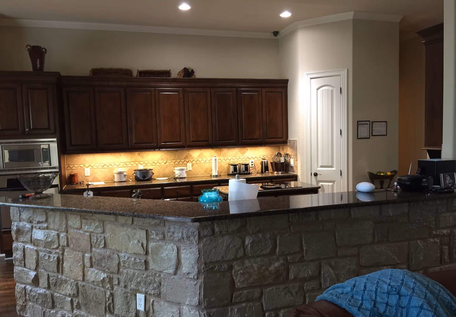 Open kitchen with a stone-faced island, dark granite countertop, and wooden cabinets under recessed lighting.