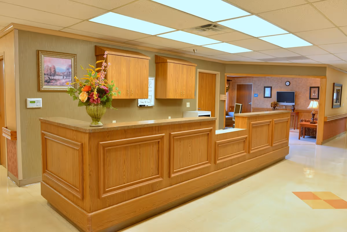 Wood-paneled reception desk in a bright lobby with a vase of flowers and a seating area in the background.