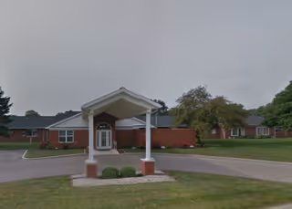 Front entrance of a single-story brick skilled nursing facility with a covered drive-through portico and surrounding lawn.