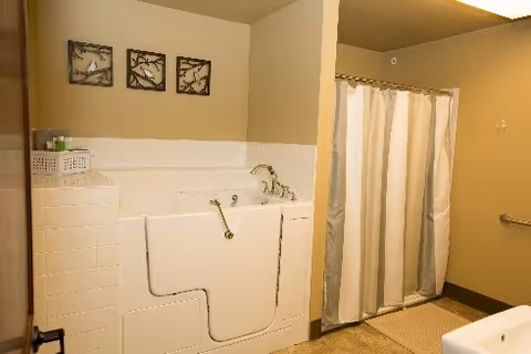 Beige bathroom featuring a white walk-in bathtub with faucet, a striped shower curtain, and decorative wall art.