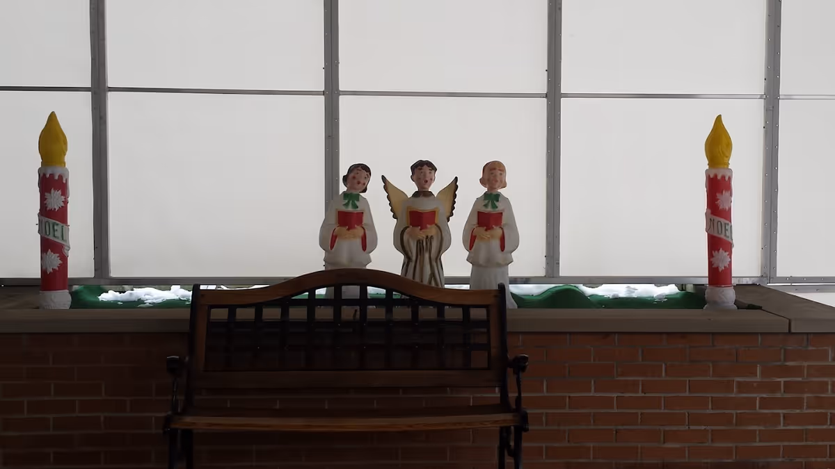 Wooden bench in front of a planter displaying three angel/choir figurines and two tall candle decorations against frosted windows.