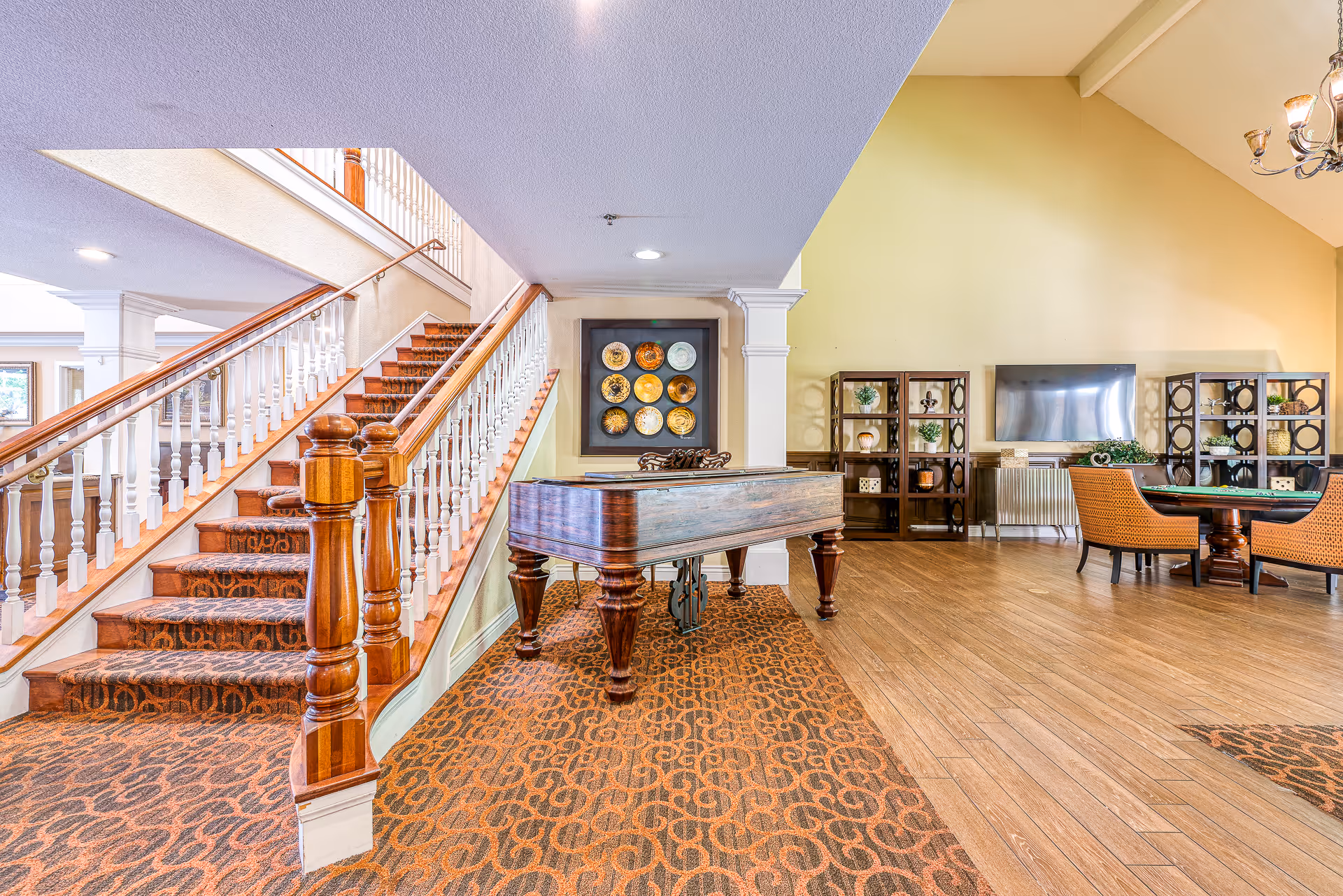 Interior common area with a carpeted staircase, a grand piano, seating area, TV, and decorative shelving.