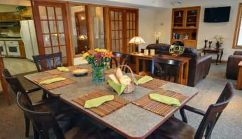 A communal dining table set with placemats and flowers in a cozy facility dining room.
