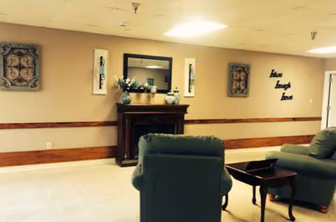 Cozy lounge at Farmerville Nursing and Rehabilitation Center with green recliners, fireplace, and decor.