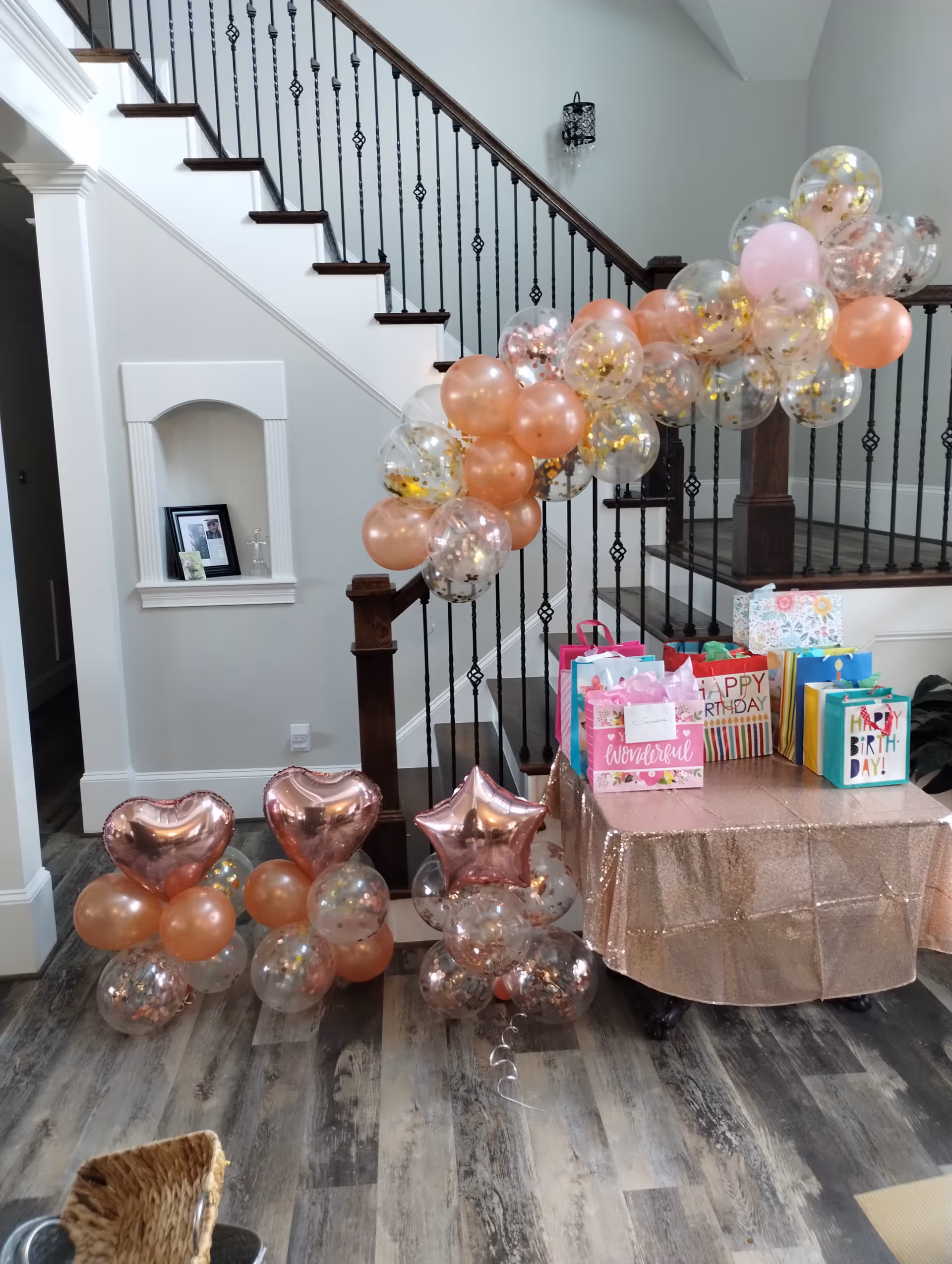 Foyer with a stairway decorated with rose-gold and clear balloons and a table full of birthday gift bags