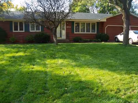 Front exterior of a single-story red brick senior living building with a green lawn.