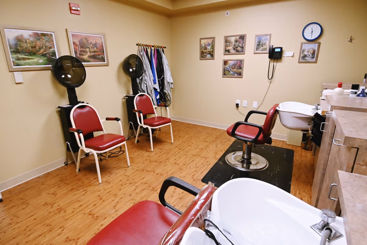 Interior salon room with red styling chairs, hooded dryers, shampoo sinks, and framed artwork on the walls.