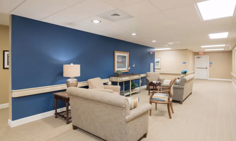 Hallway lounge with beige sofas and chairs arranged around side tables in front of a blue accent wall.