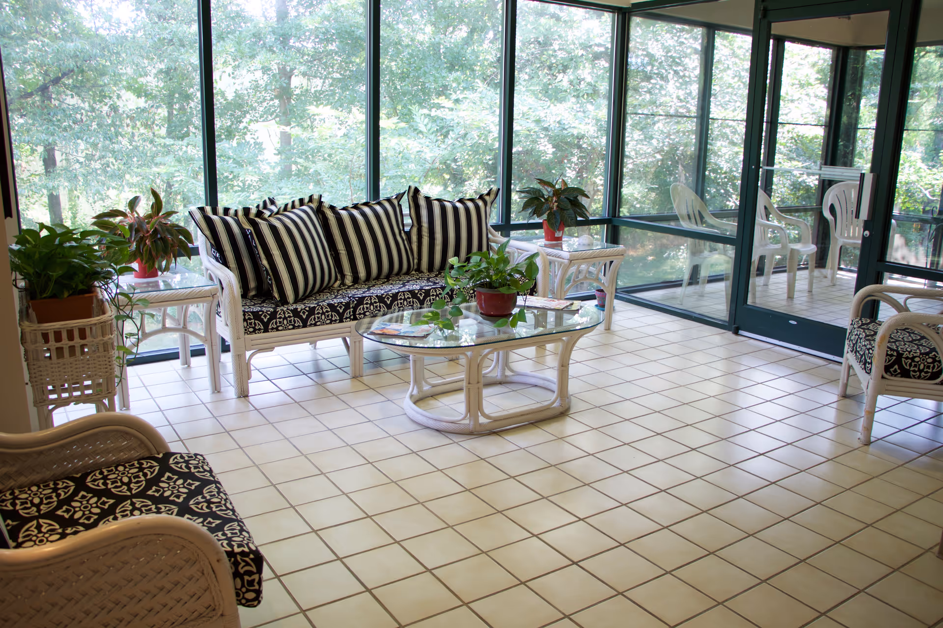 Sunlit indoor lounge with white wicker seating, striped cushions, and potted plants.