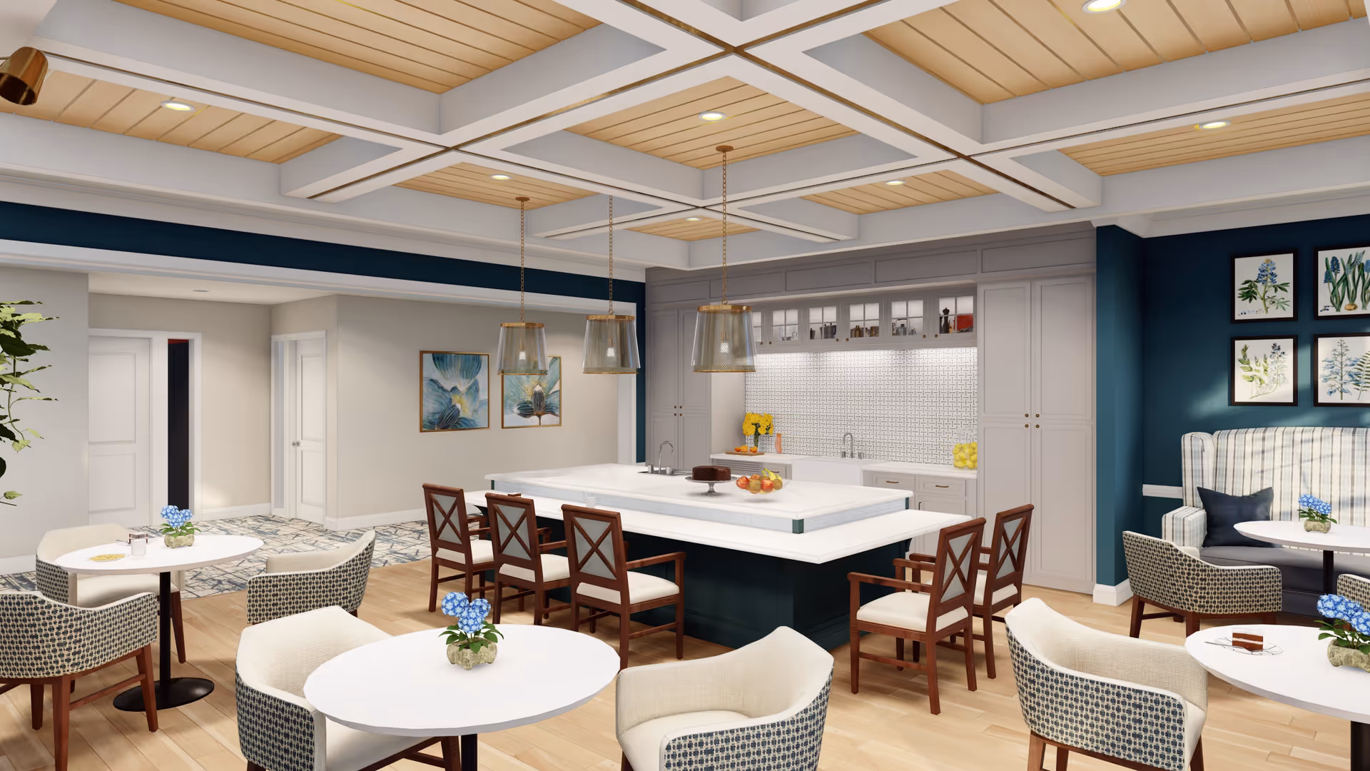 A modern senior living dining area with multiple round tables and cushioned chairs, a large kitchen island with wooden chairs, pendant lights hanging from a coffered ceiling, and a kitchen area with white cabinets and a tiled backsplash. The walls are painted in a combination of teal and beige, with framed botanical artwork and a plaid upholstered bench along one wall.