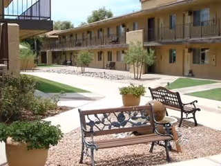 Outdoor courtyard of a two-story senior living facility with benches, potted plants, walkways, and second-floor balconies.