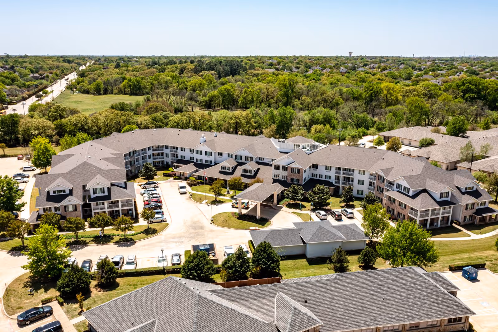 Aerial view of a large multi-wing senior living complex with parking areas, driveways and surrounding trees.