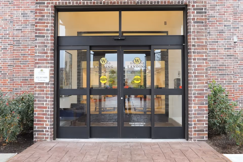 Front glass double-door entrance of an assisted living facility with a brick facade and 'Landing' signage.