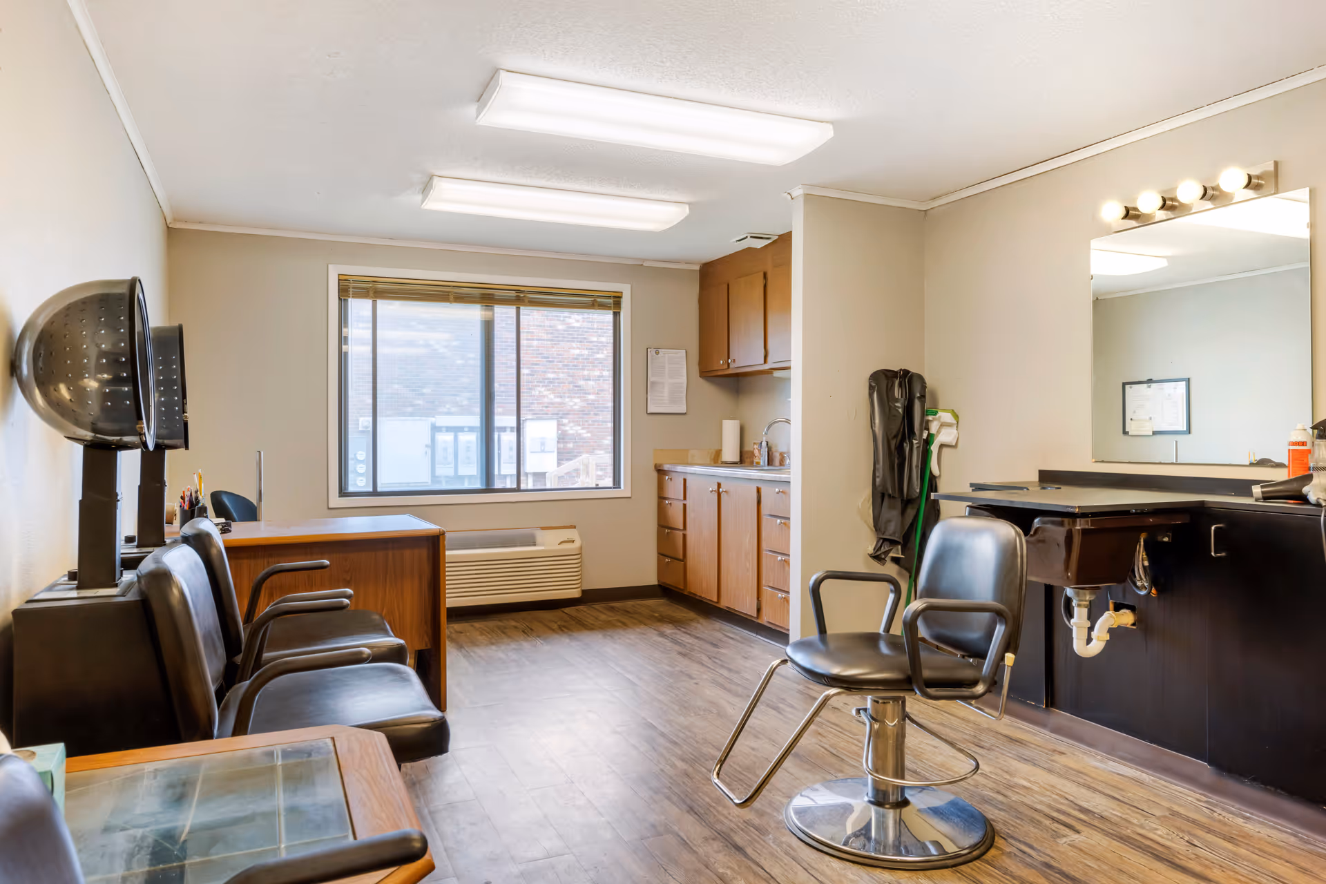 Interior salon room with styling chairs, a hooded hair dryer, sink and counter under a window.
