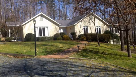 Single-story senior living building with front lawn, pathway, and surrounding trees.