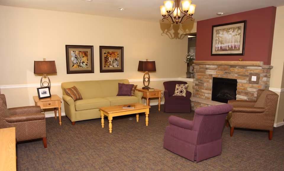Cozy common room with a sofa, several armchairs, coffee table, lamps and a stone fireplace.