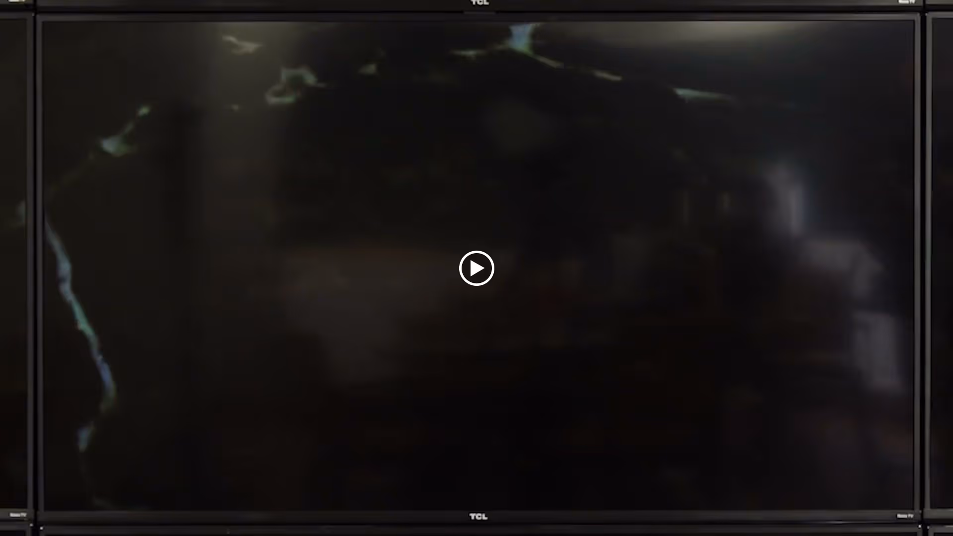 Large dark flat-screen television with a centered play icon and faint reflections on the screen.