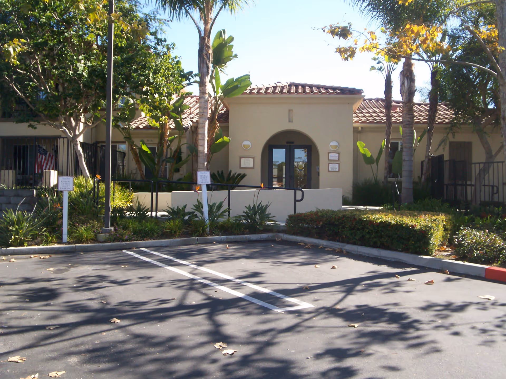 Exterior view of a building entrance at Vintage Shores with a tiled roof, surrounded by trees and plants, and a parking area in the foreground with signs indicating rental guest parking.