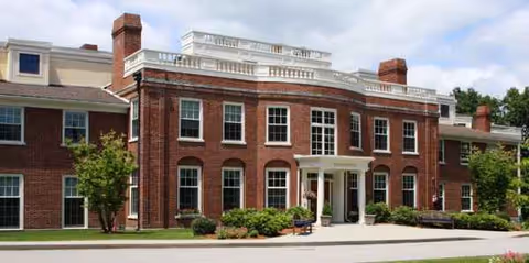 Brick building with white columns and entrance stairs, manicured landscaping outside.