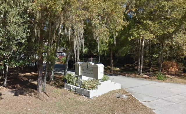 Entrance sign for Caring Village of Forest Glen among trees by a paved driveway.