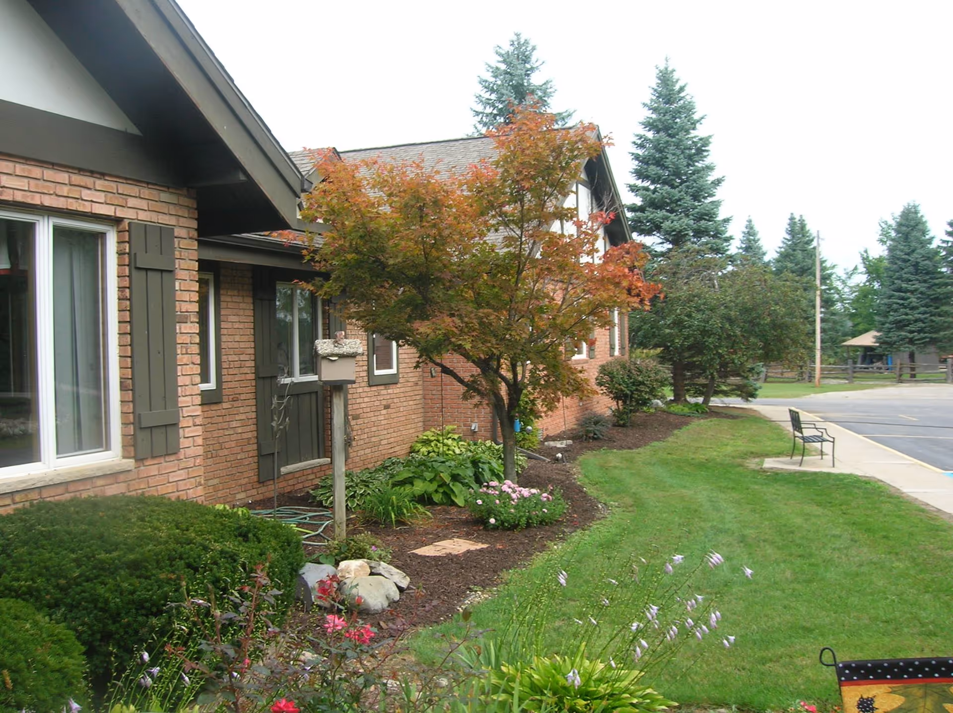 Brick building front with landscaped lawn, a small tree, walkway and a bench outside.