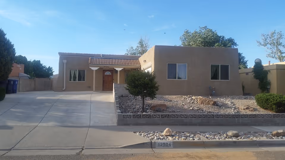 Single-story stucco house with a driveway and rock landscaping under a clear blue sky.