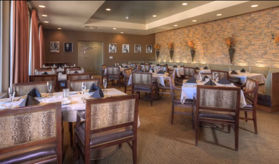 Interior dining room with multiple set tables, upholstered chairs, and a stone-accent wall.
