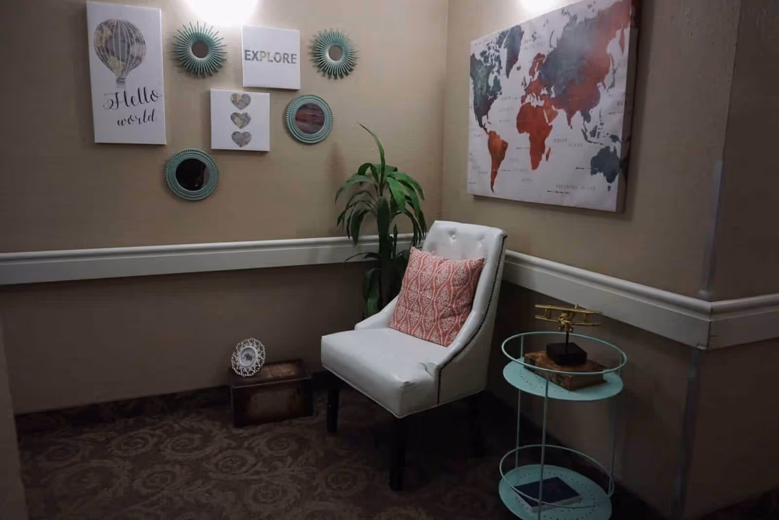 Small seating nook in a hallway with a white upholstered chair, decorative wall art, a potted plant, and a round side table.