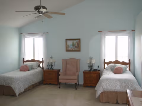 Twin beds with nightstands flank a central chair in a pastel blue bedroom.
