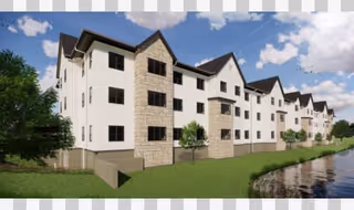 Exterior view of a multi-story residential building with white siding and stone accents, situated next to a body of water under a partly cloudy sky.