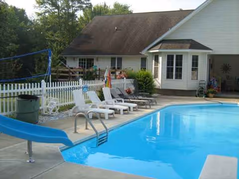 Outdoor pool area with lounge chairs, a slide, and a white picket fence.