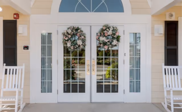 Front entrance with white double glass doors decorated with floral wreaths and rocking chairs on the porch.