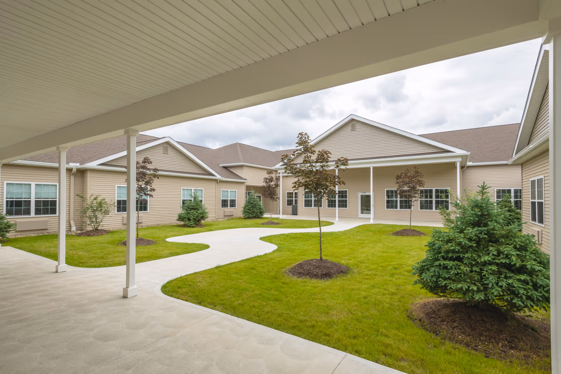 Covered walkway overlooking a grassy courtyard with young trees and a surrounding beige single-story building.