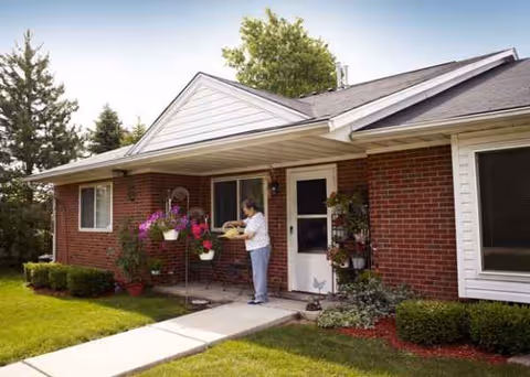 Brick exterior of a single-story senior living home with a front porch and flowering plants.