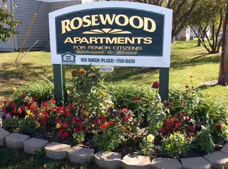 Front sign reads Rosewood Apartments for Senior Citizens, framed by blooming flowers and a green lawn.