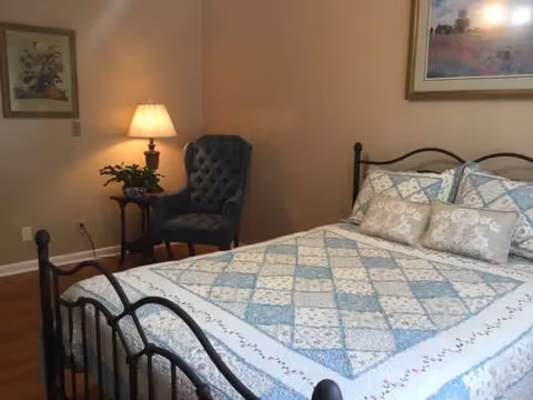 Cozy bedroom featuring a metal bed, quilted bedding, lamp, and a blue upholstered chair.