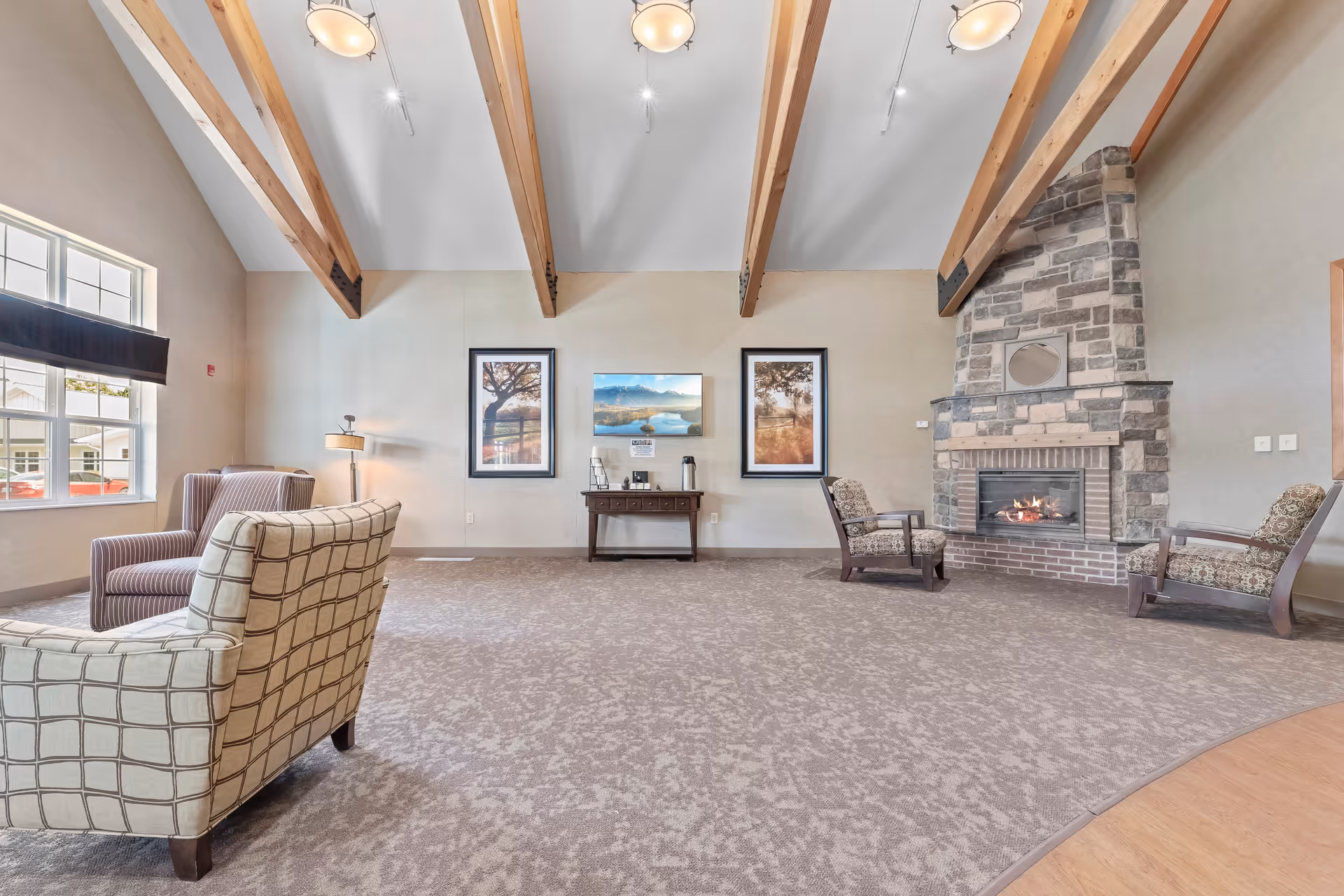 Spacious senior living lounge with exposed wood beams, upholstered chairs, a table, and a stone fireplace.