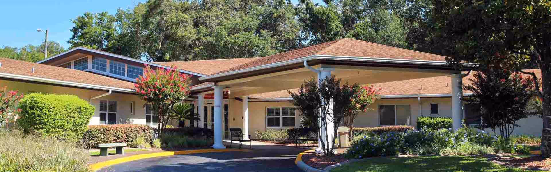 Front entrance of a single-story building with a covered portico, columns, and landscaped grounds.