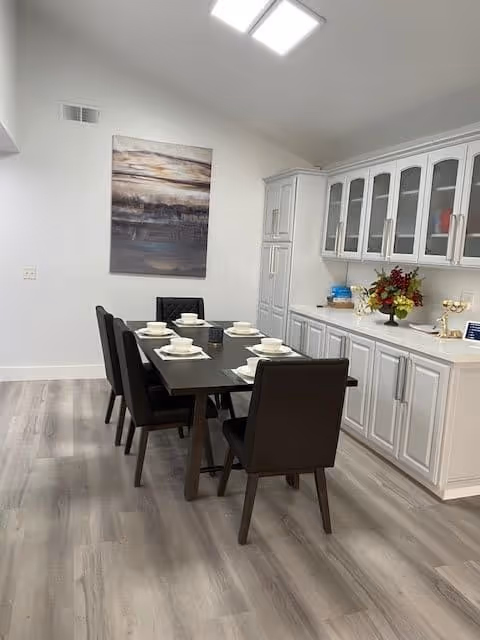 Modern dining room with a dark wood table set for six, brown upholstered chairs, white built-in cabinetry, and a large wall painting.