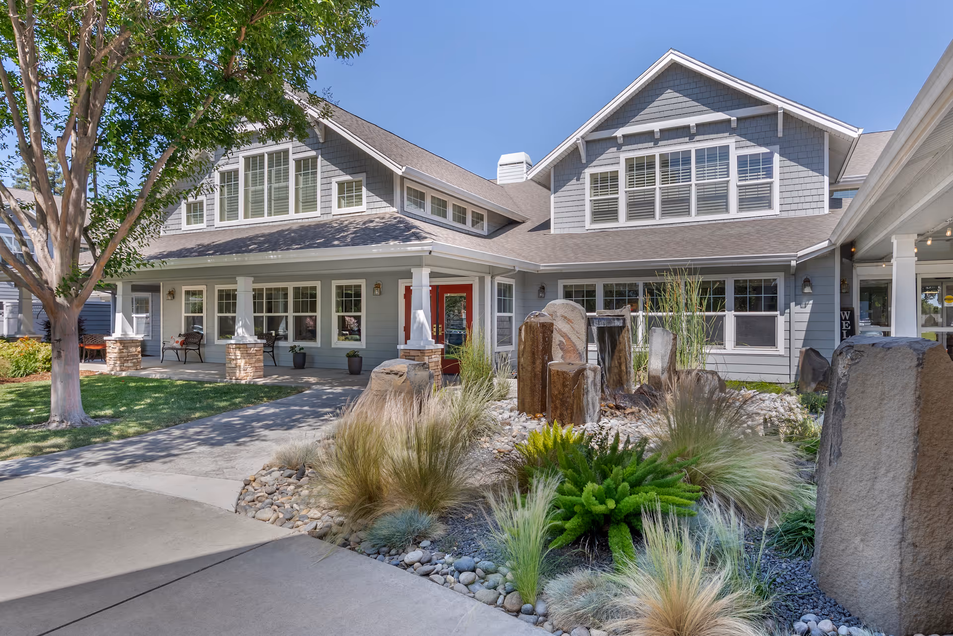 Front exterior of a two-story residential building with a covered porch, landscaped rock garden, and a stone water feature at the entrance.