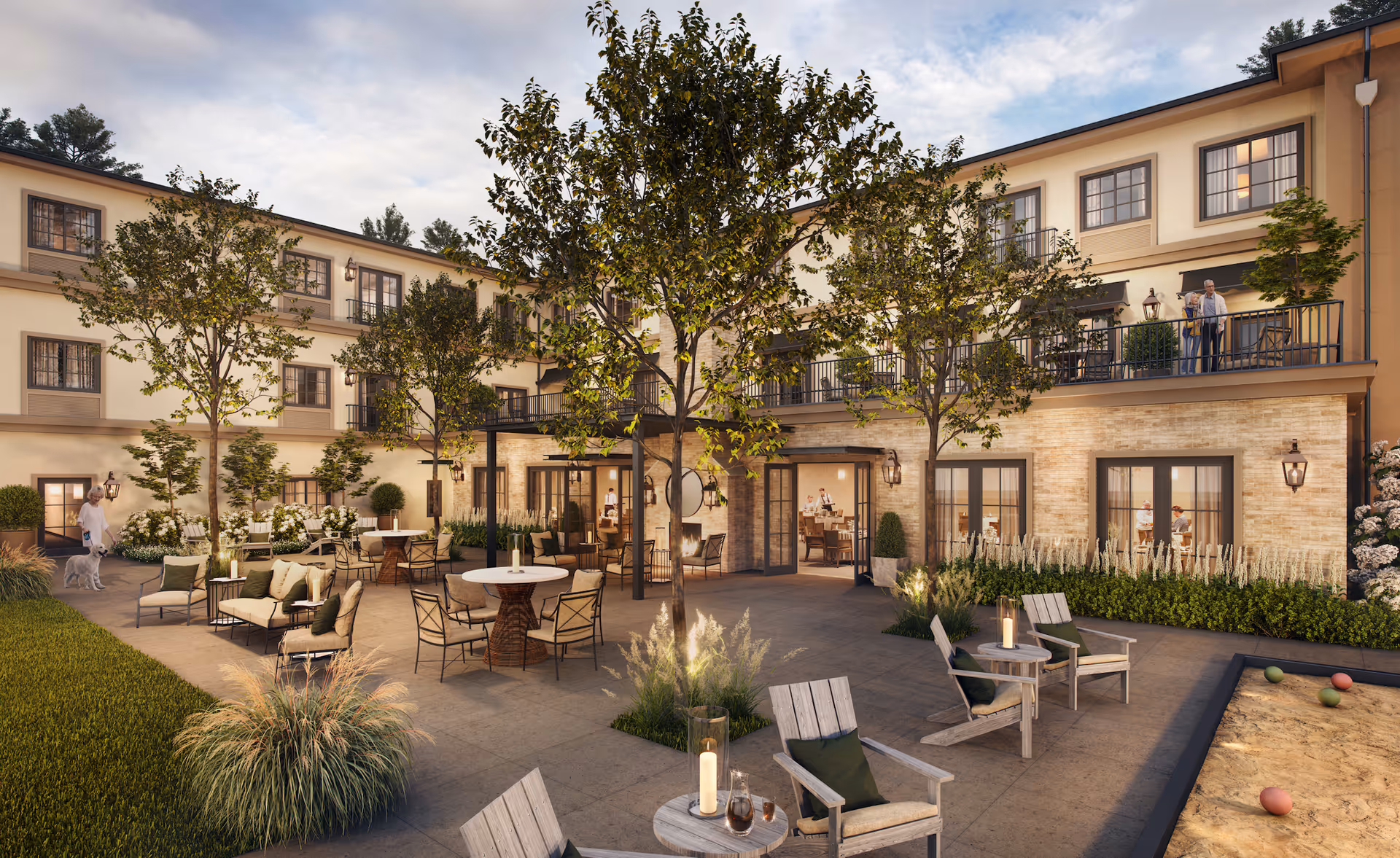 Outdoor courtyard area of Weatherly Inn Renton with seating arrangements including tables and chairs, trees, and plants. The building has three stories with multiple windows and balconies. People are seen enjoying the outdoor space, including a person walking a dog and two people standing on a balcony.