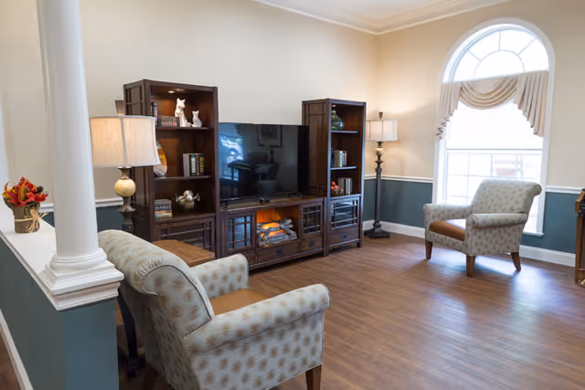 Cozy living room in Lavender Hills Front Royal Campus with armchairs, TV, and arched window.