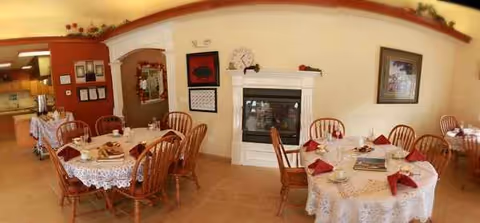 Sunlit dining room with round tables, red napkins, lace cloths, and a fireplace.